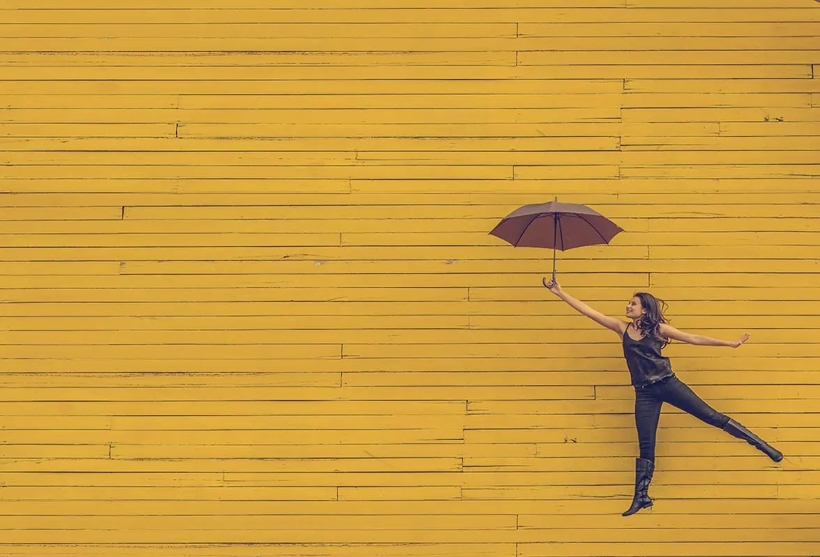 Une personne qui flotte devant un mur jaune, accrochée à un parapluie